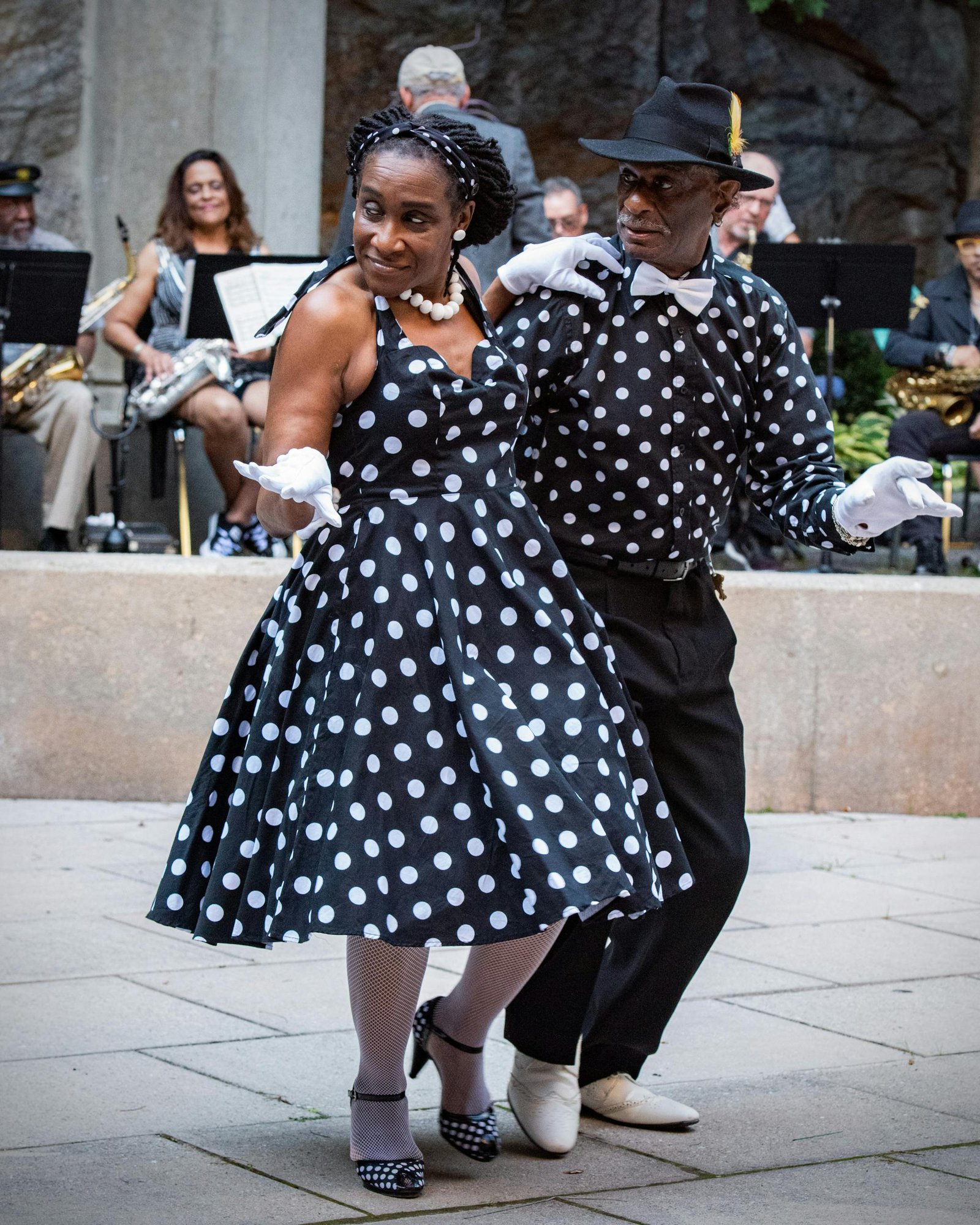 A fashionable couple swing dancing outdoors in New York City, showcasing vibrant polka dot outfits.