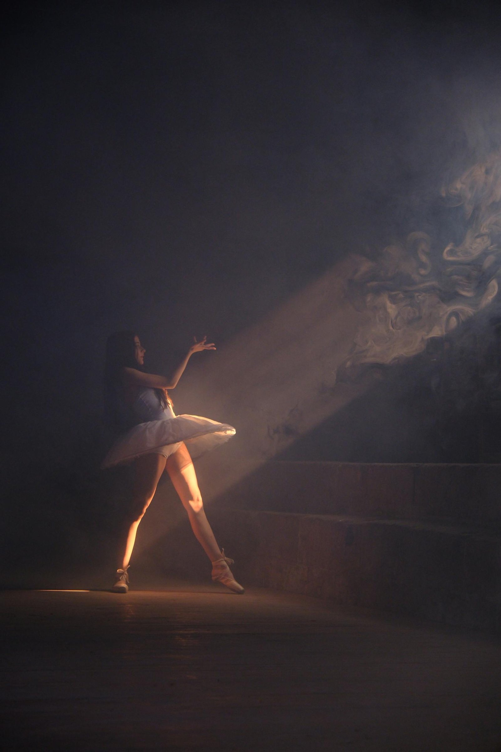 A graceful ballerina performing a dance in dramatic lighting with shadows and smoke.