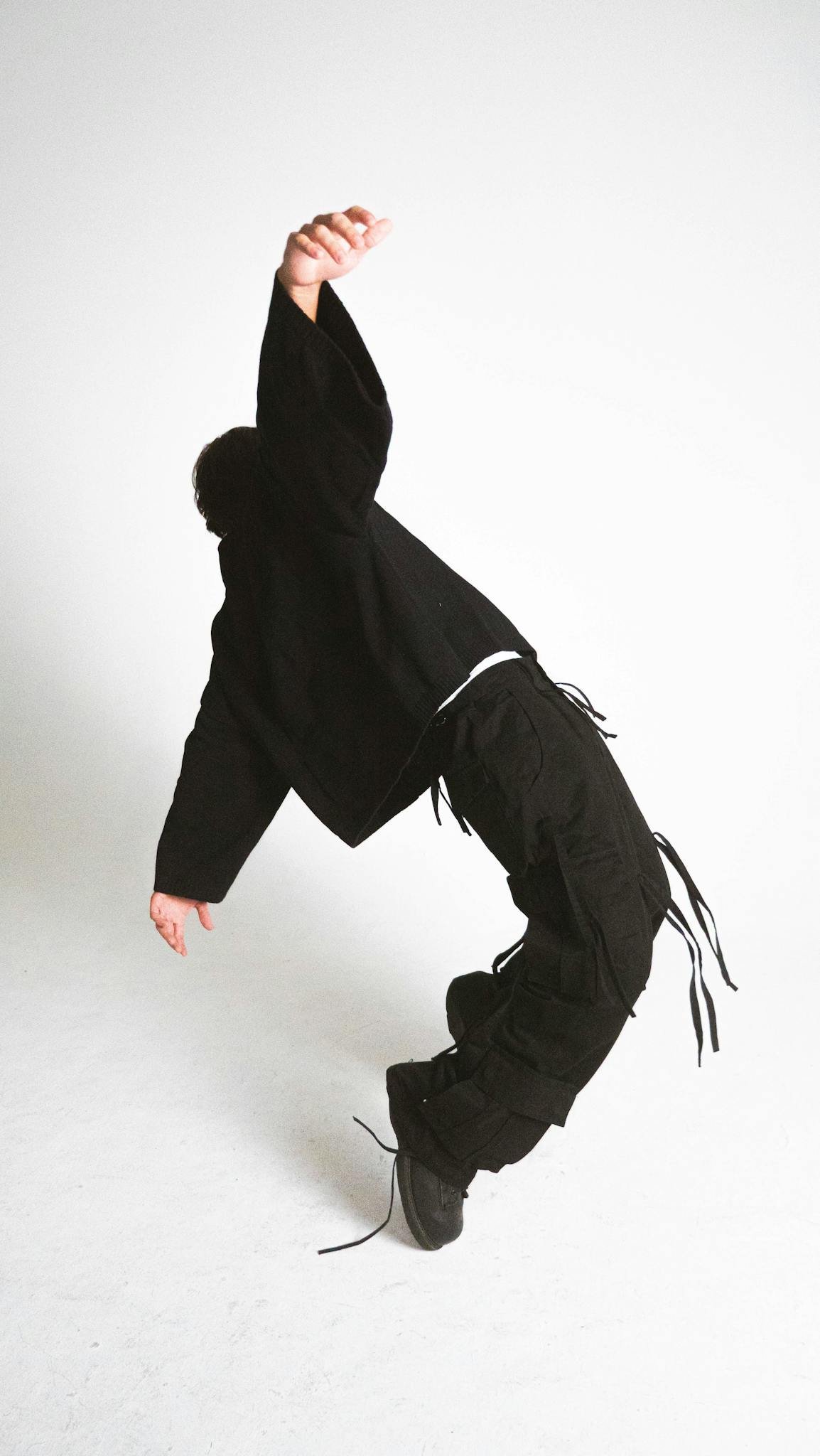 Creative and dynamic pose of a person wearing black clothing on a white background.