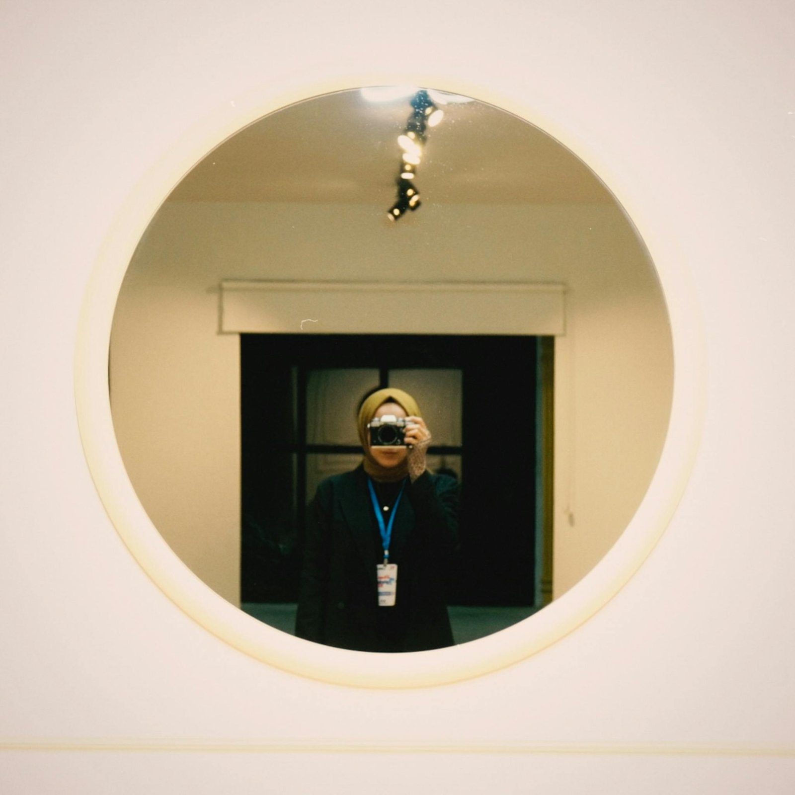 Creative selfie of a woman capturing her reflection in a round mirror with a film camera.