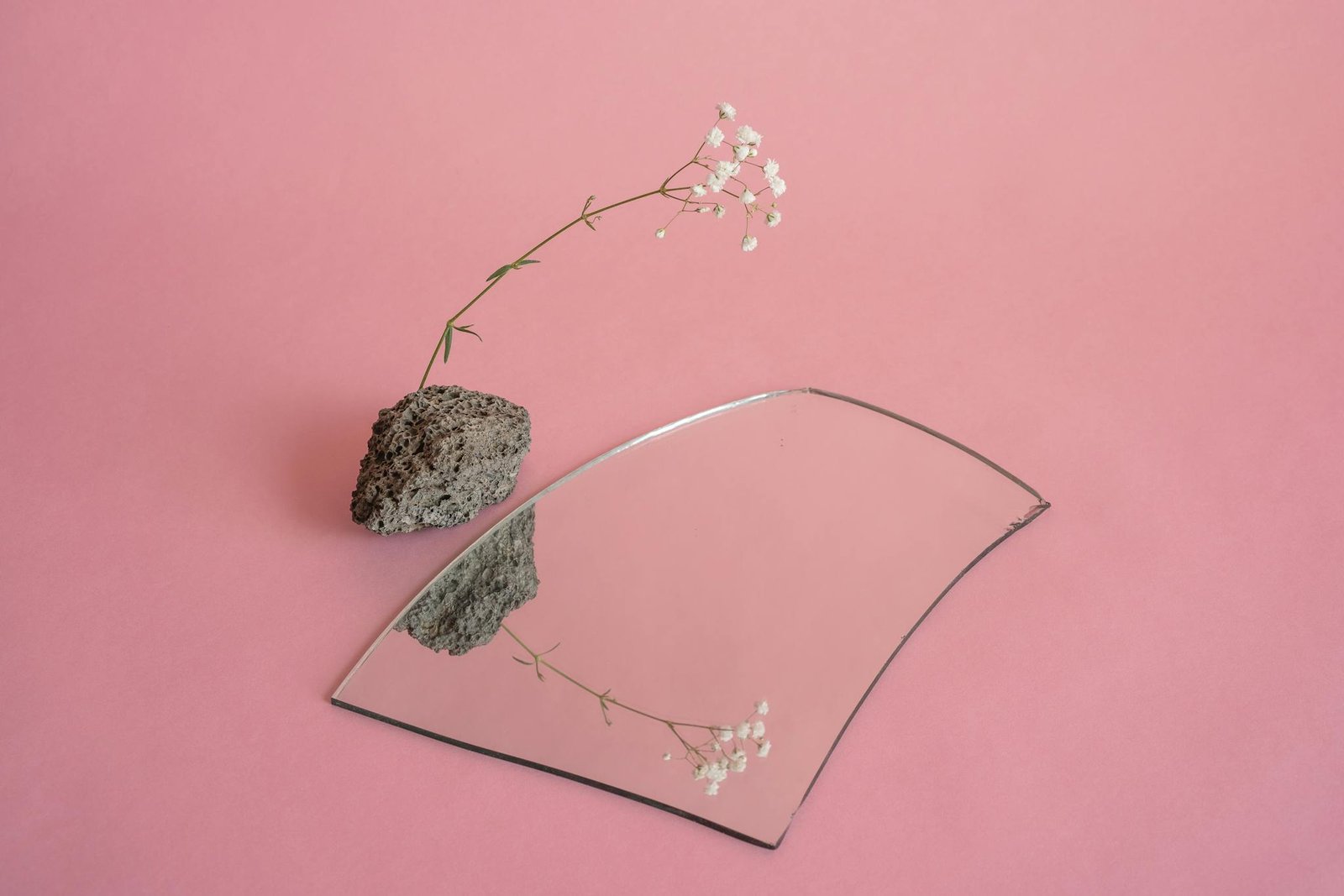 Gypsophila flower and stone reflected in a broken mirror on pink background.
